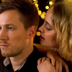 Kobieta szepcze komplement mężczyźnie do ucha na tle nastrojowych świateł