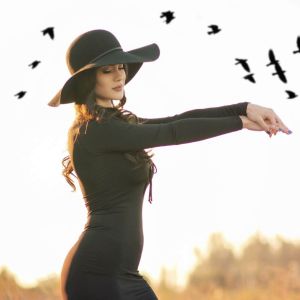 Kobieta w czarnym kapeluszu i sukience na tle nieba z lecącymi ptakami – wiosenne wróżby i ornitomancja