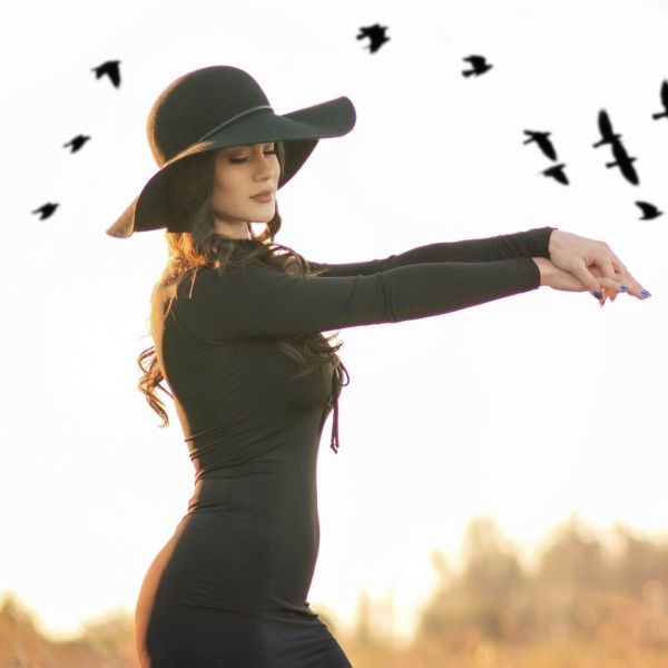 Kobieta w czarnym kapeluszu i sukience na tle nieba z lecącymi ptakami – wiosenne wróżby i ornitomancja