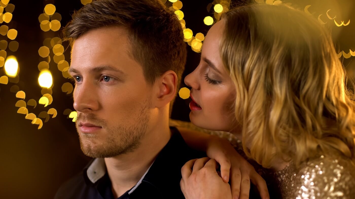 Kobieta szepcze komplement mężczyźnie do ucha na tle nastrojowych świateł